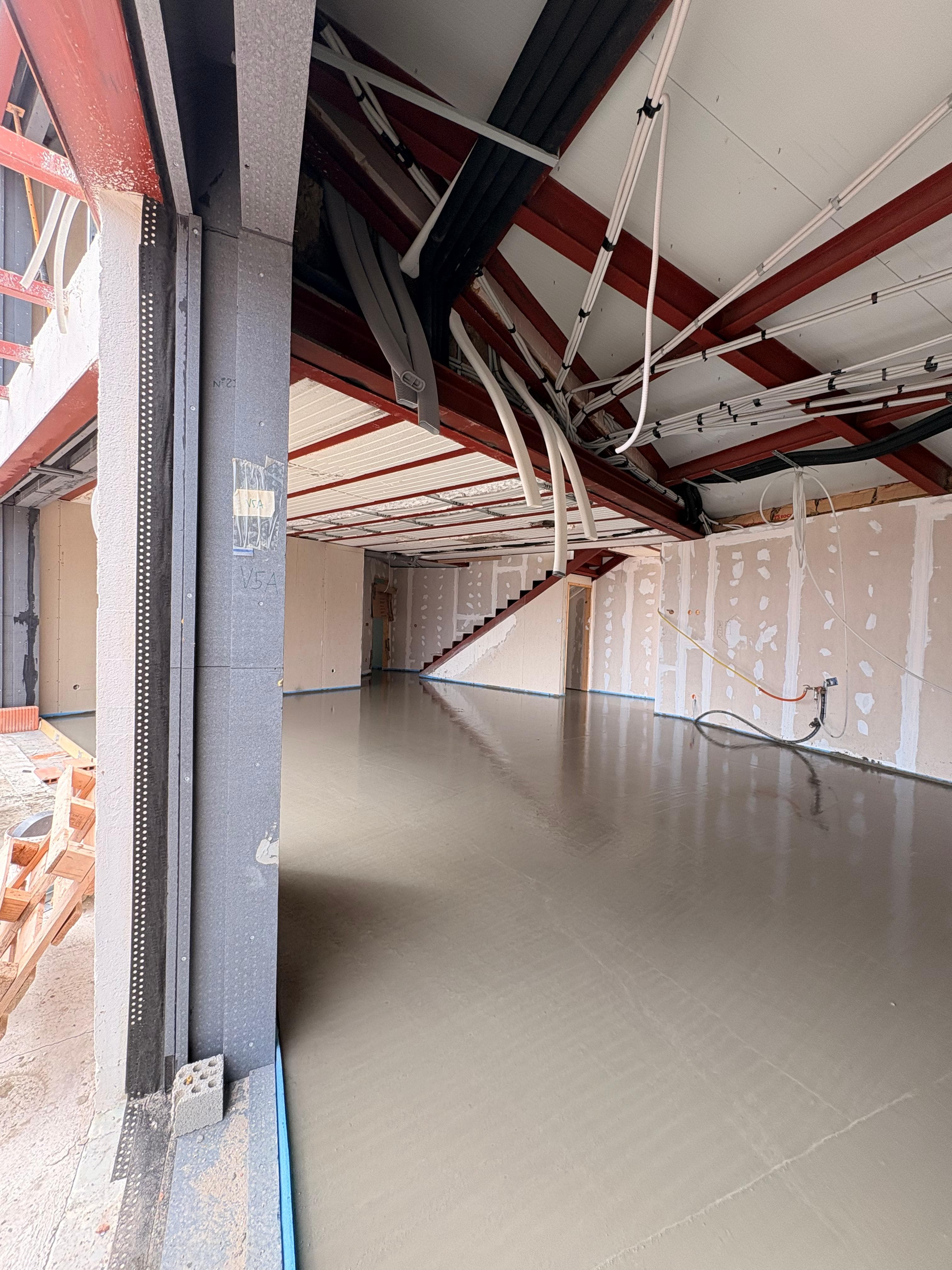 Suelo de cemento recién vertido en una habitación en construcción con vigas de acero.