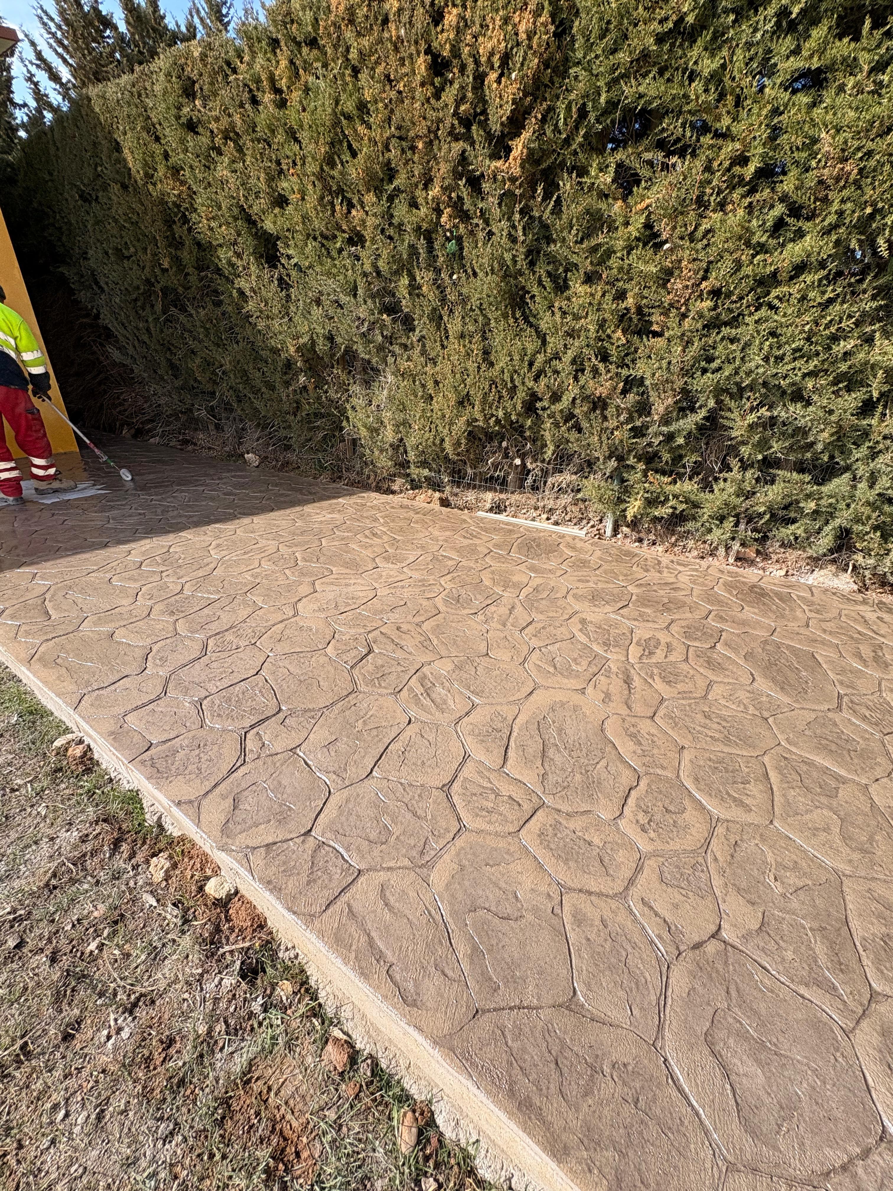 Suelo de hormigón impreso con diseño de piedra natural junto a un seto verde.