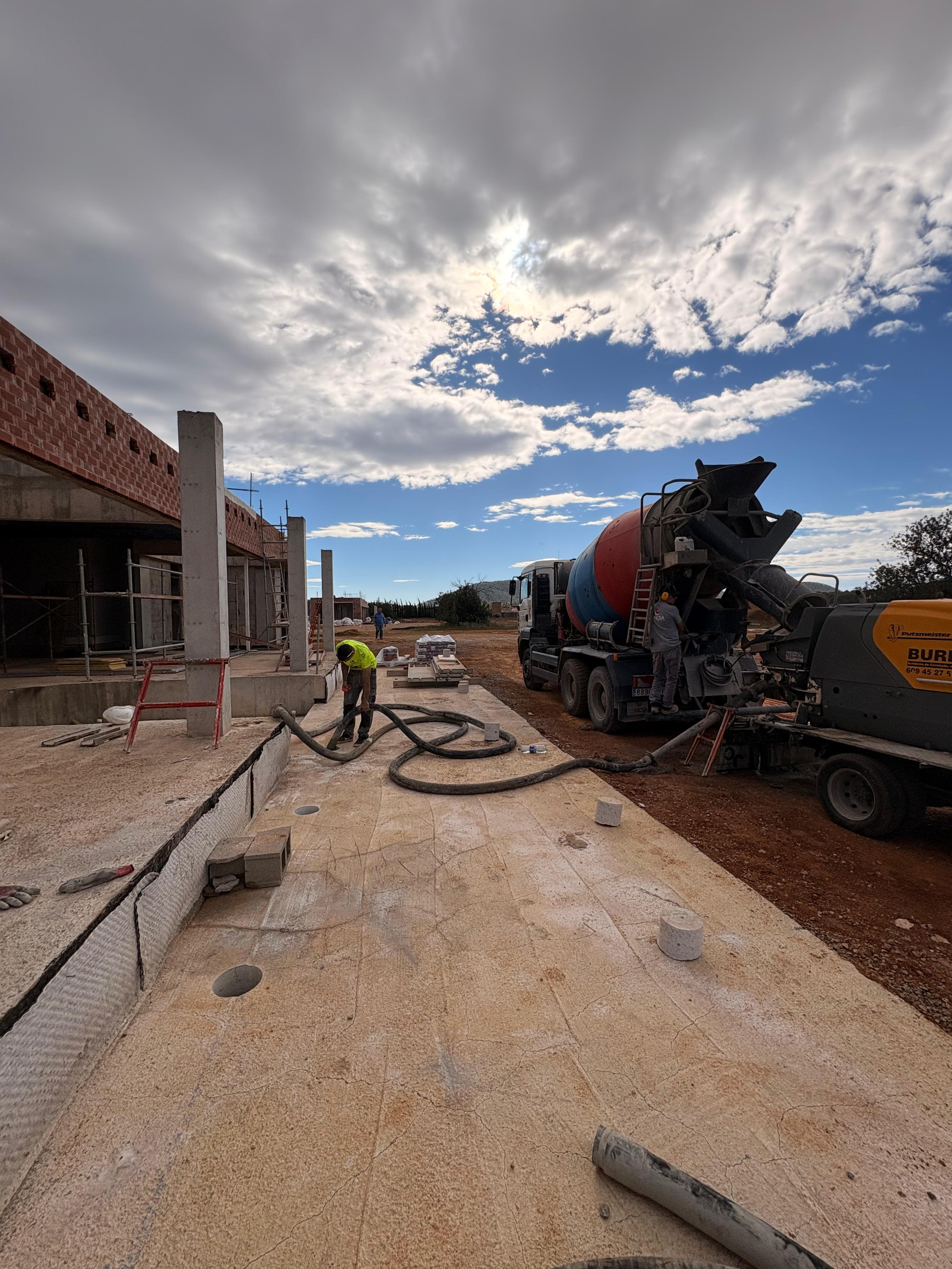 Camión hormigonera y bomba de concreto en una obra de construcción con obreros trabajando.