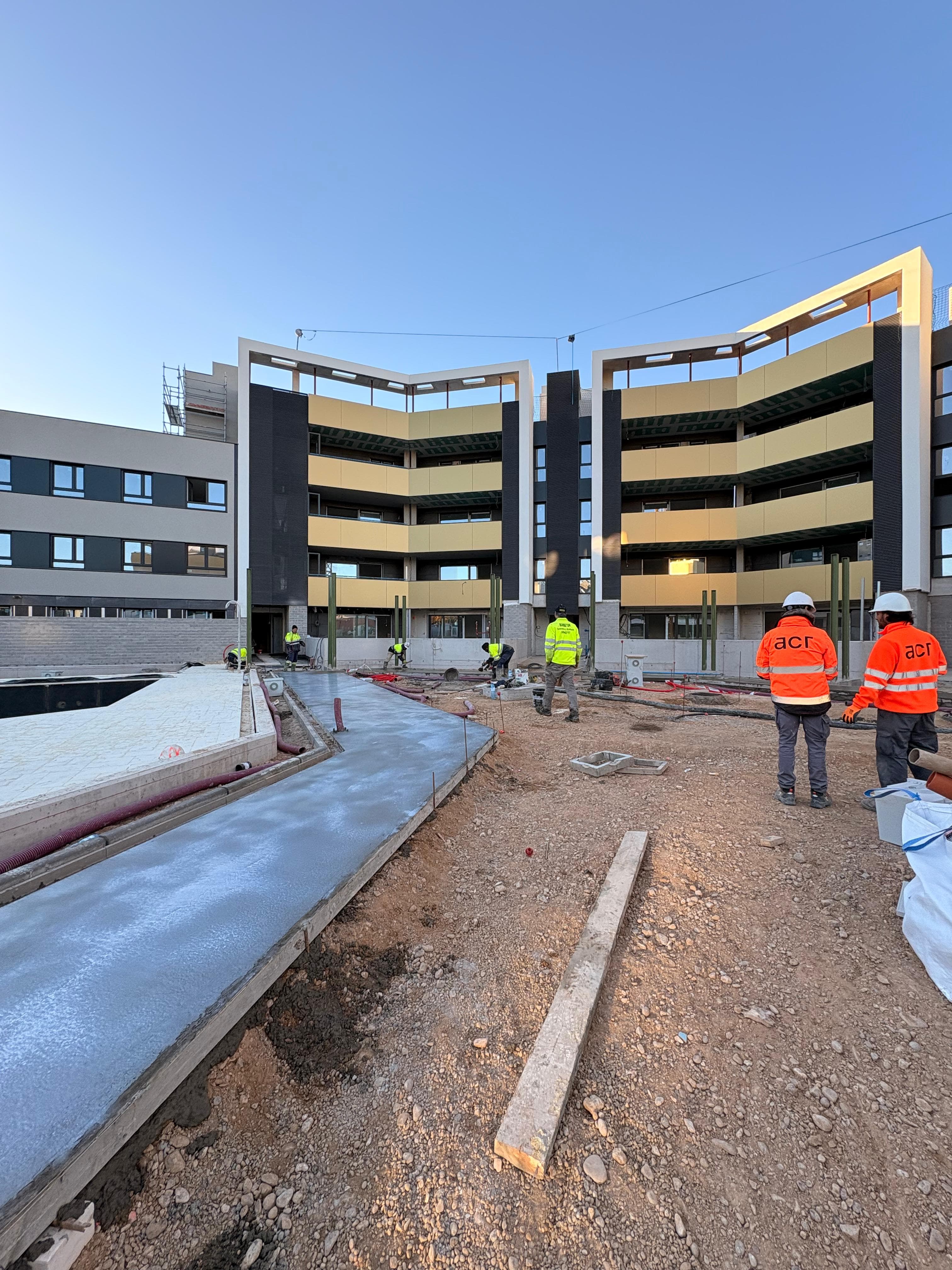 Obreros trabajando en un edificio moderno amarillo y gris con camino de hormigón fresco.